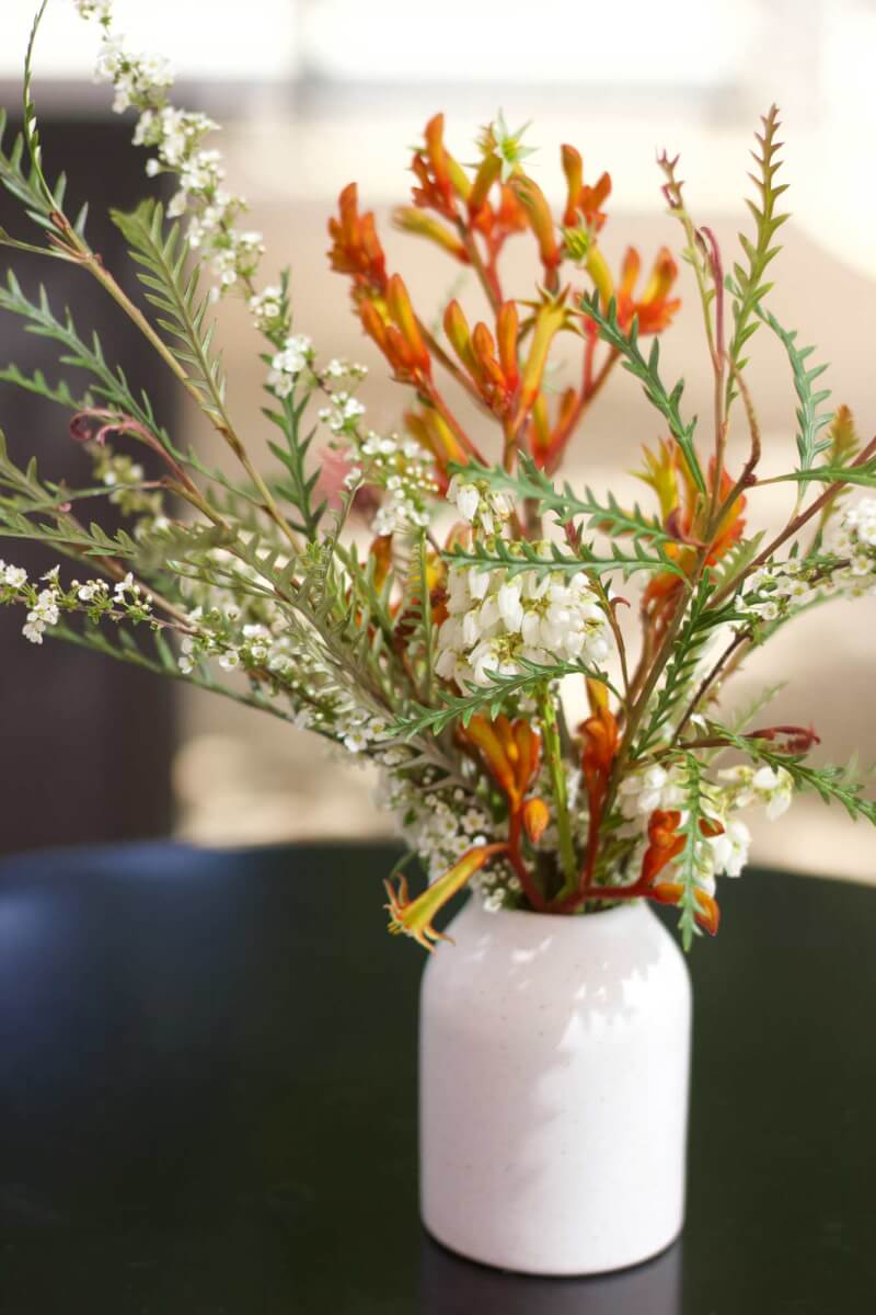 a white vase filled with bright orange and yellow flowers on top of a table at a winery event