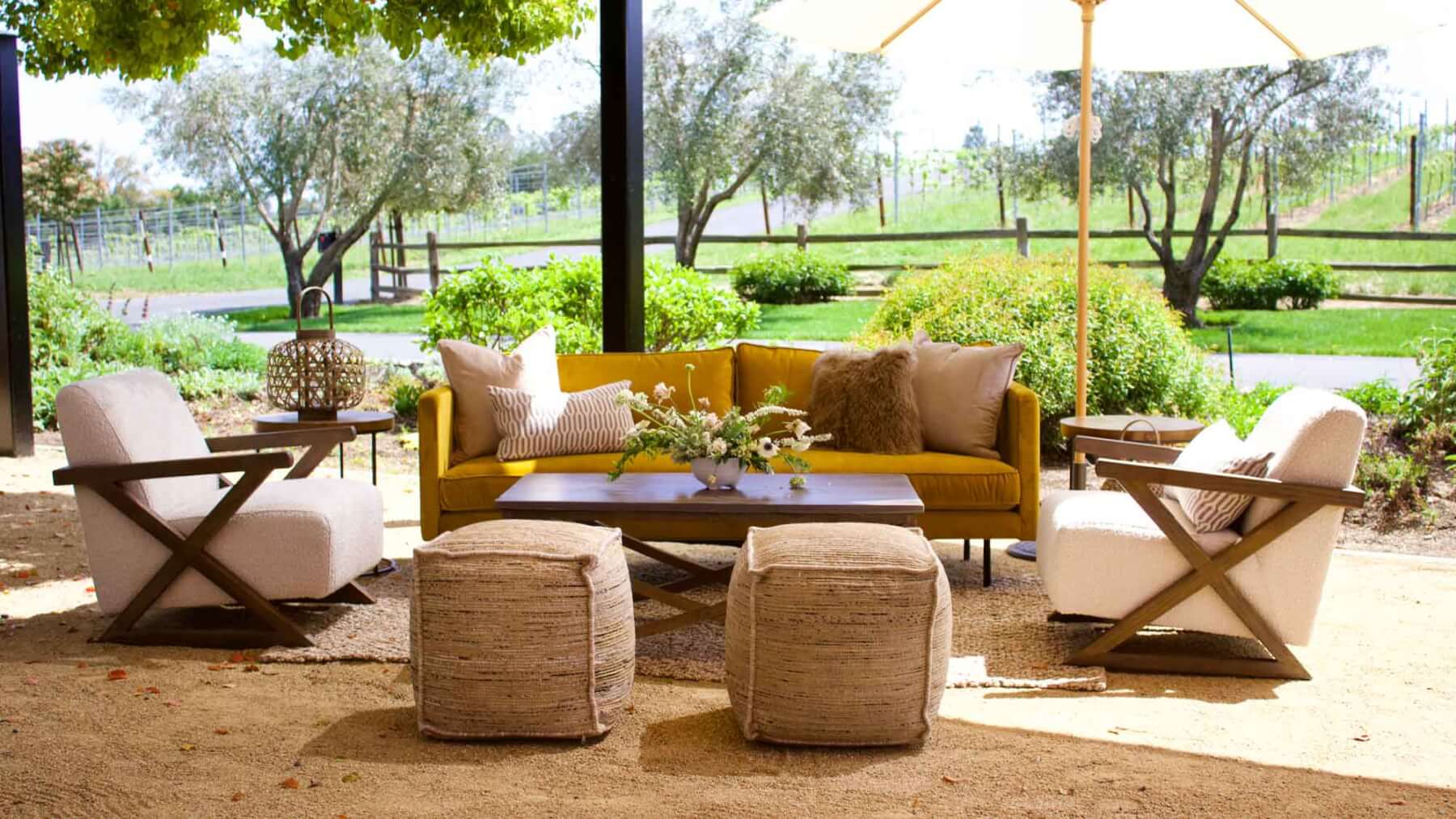an outdoor winery event sitting area filled with furniture and a floral arrangement under an umbrella.
