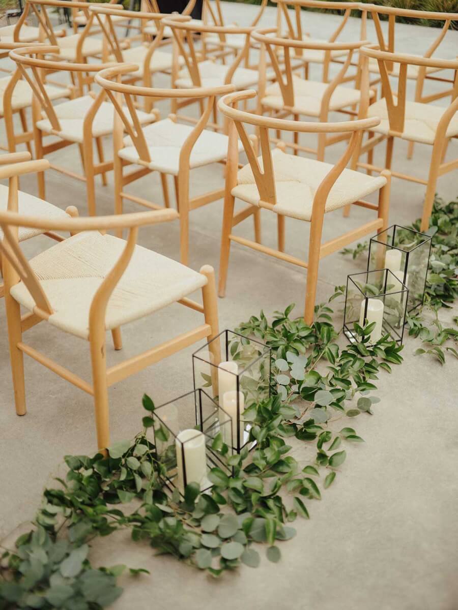 Candles line the wedding chairs, surrounded by greenery.