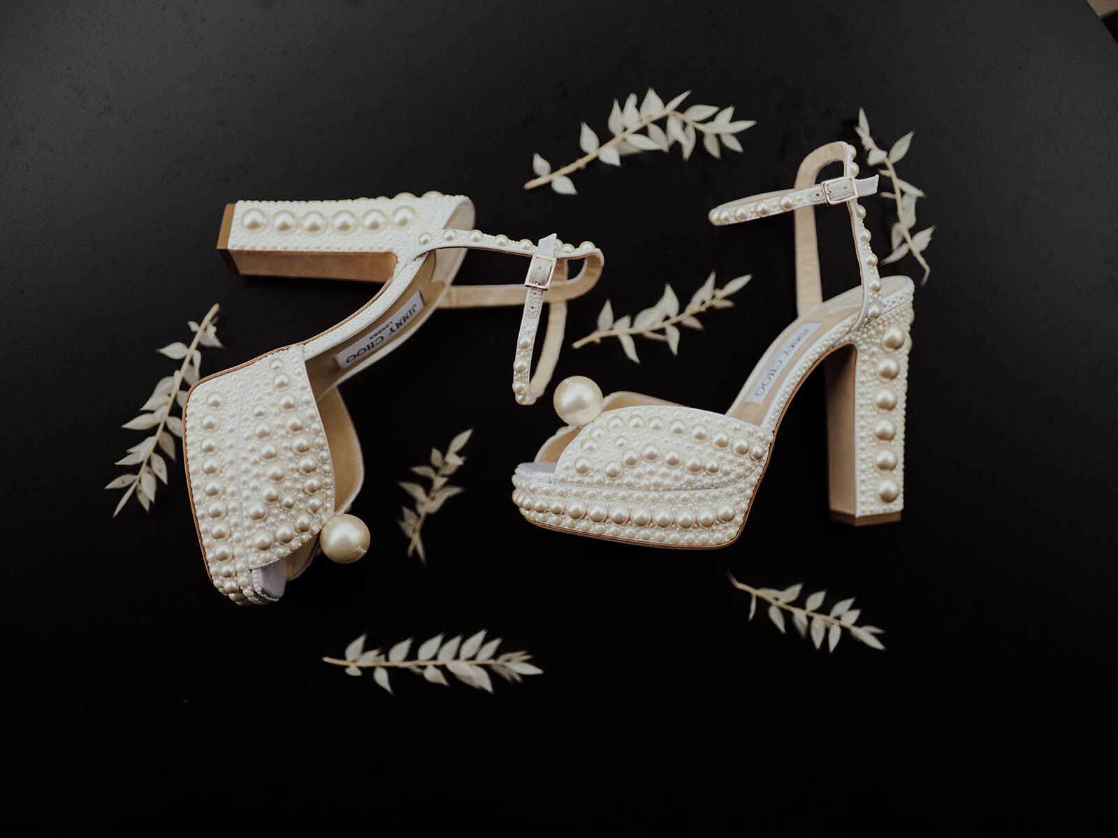 A pair of white high heeled wedding shoes on a black background.