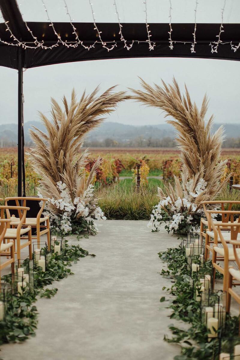 looking down the aisle at the pampas grass wedding arch with the vineyard in the background