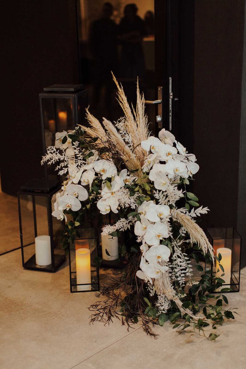 candles in black hurricane enclosures with a large pampas grass and white flower arrangement