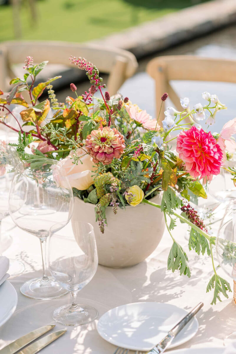 An outdoor wedding table setting with gorgeous brightly-colored flowers in a bowl.