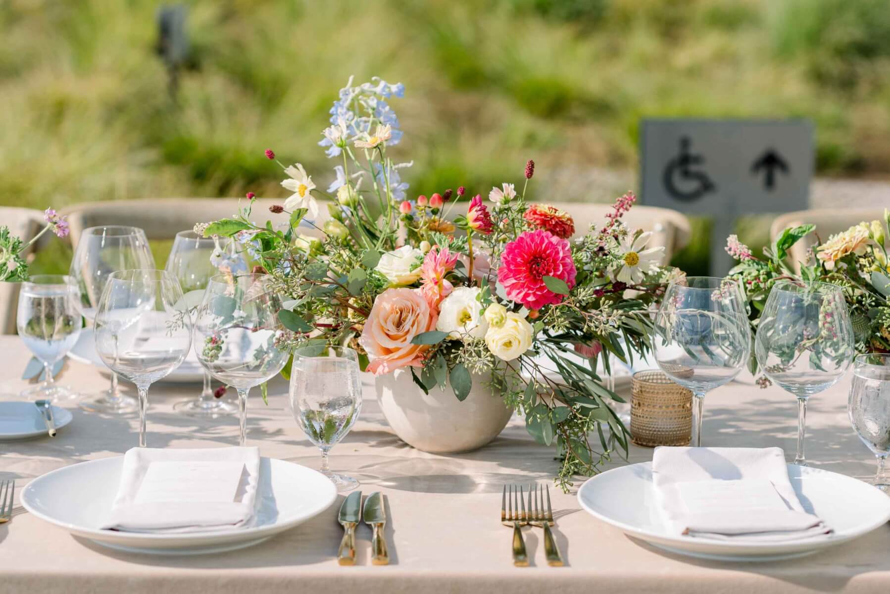 An outdoor wedding table set with a brightly-colored flowers in a rounded stone vase.
