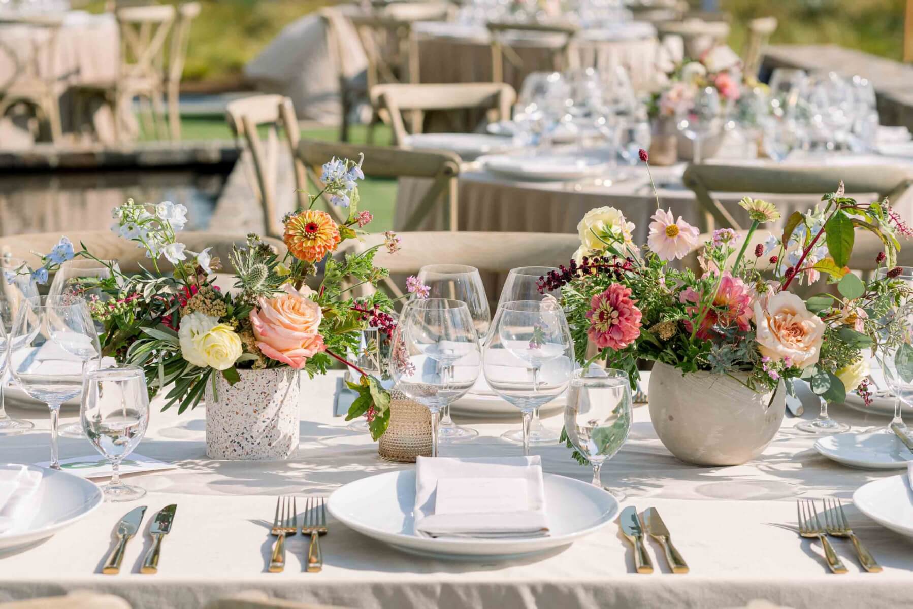 Outdoor wedding tables set with bouquets in vases.
