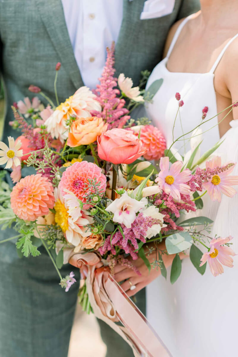 Close up of the bridal bouquet in playful colors of coral, pink, and orange with pink ribbon.