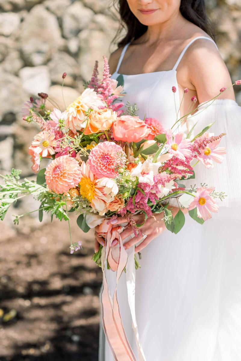 The bride holding the wedding bouquet in playful colors of coral, pink, and orange with pink ribbon.