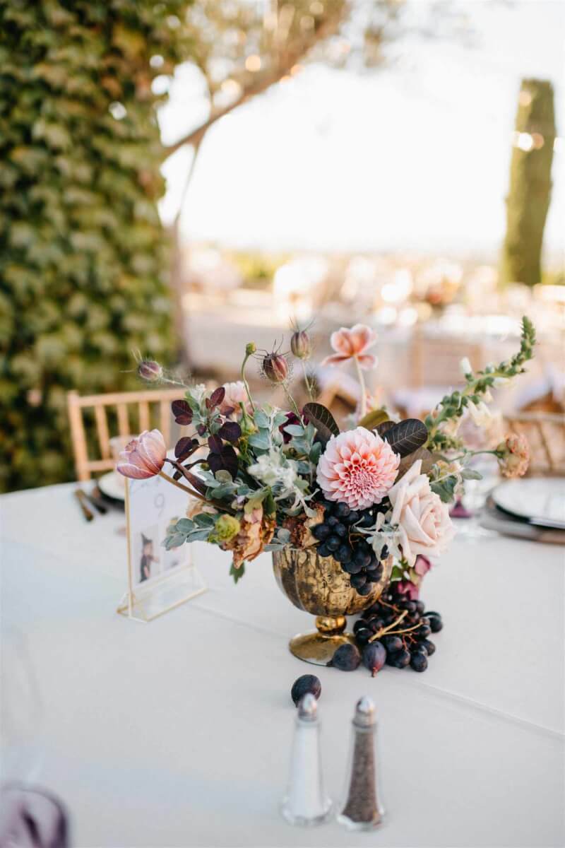 An elegant wedding table set with a floral arrangement in a gold chalice, accented with grapes from the local harvest.