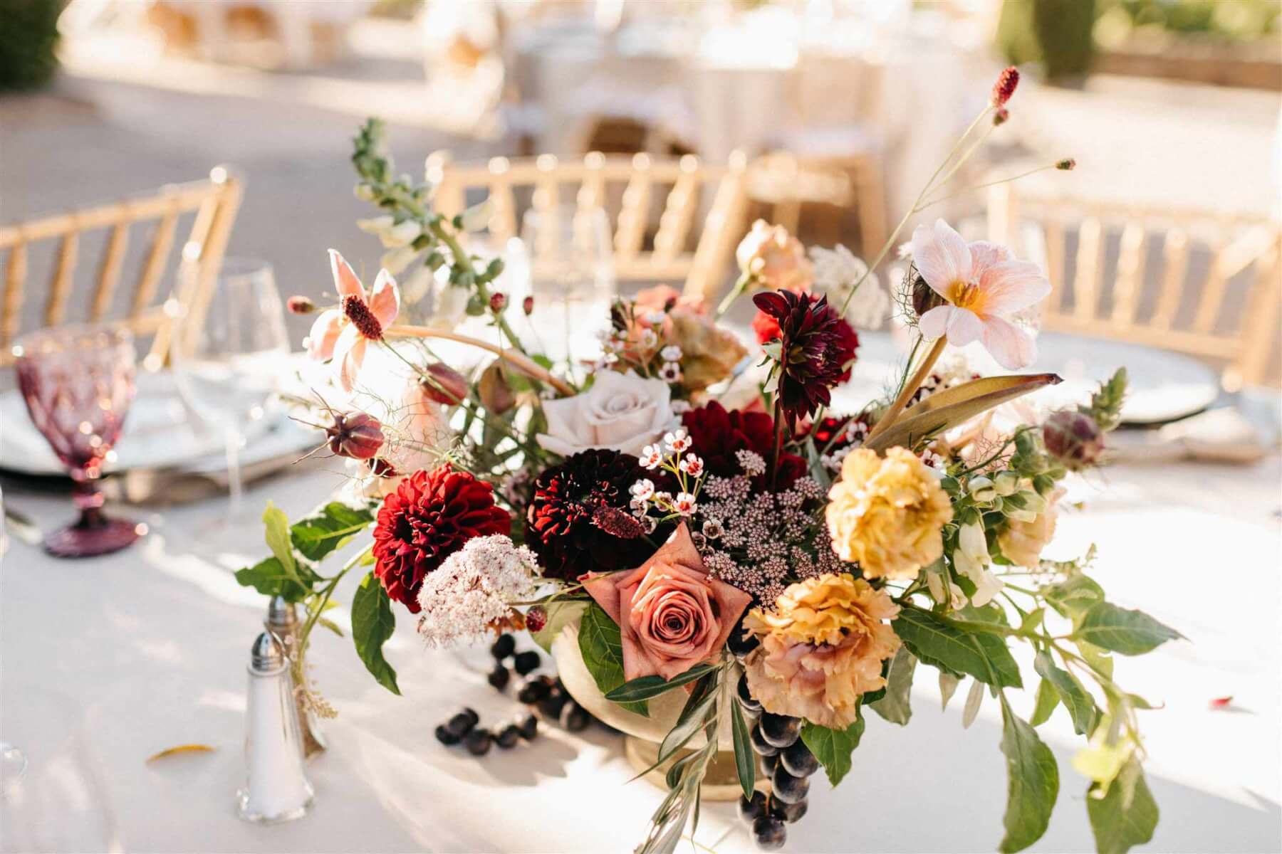 Close up of an elegant floral arrangement on the wedding table with flowers in deep plum, light blush, peach, and greenery.