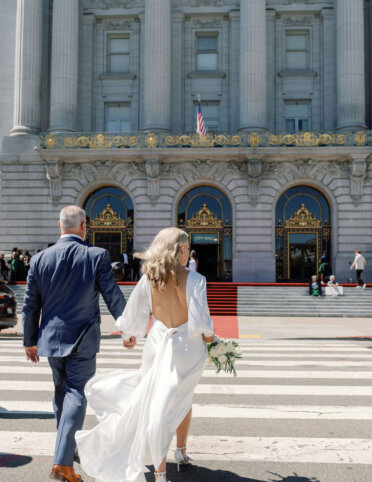 The bride and groom holding hands and crossing the street towards an San Francisco City Hall
